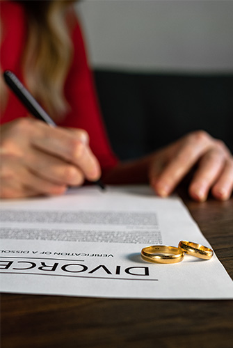 Lady signing a Divorce document with wedding rings on the page
