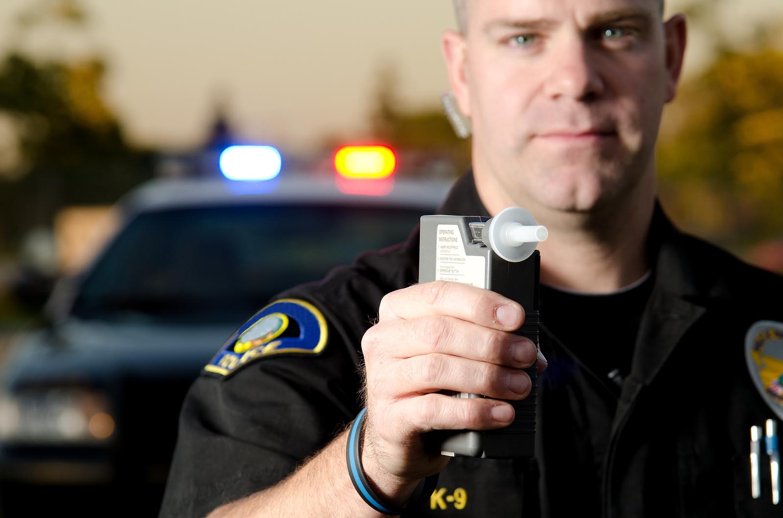 A police officer holding a breath test machine with his police car in the background for DUI charges